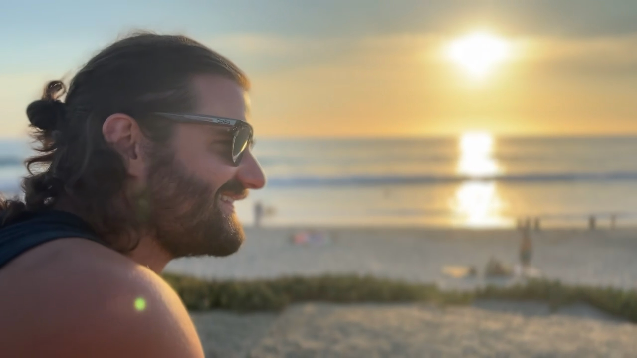 Matt in profile at the beach, looking out at a sunset over the ocean